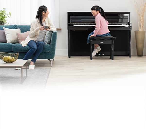 Young pianist playing Yamaha upright piano, while family enjoys time in modern living room setting.