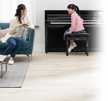 Child playing Yamaha upright piano with a woman nearby, showcasing elegant design and family-friendly music space.
