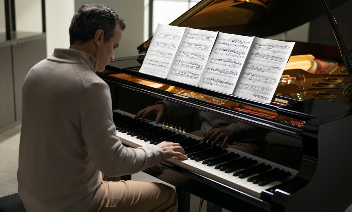 An older man in a suit playing a grand piano.
