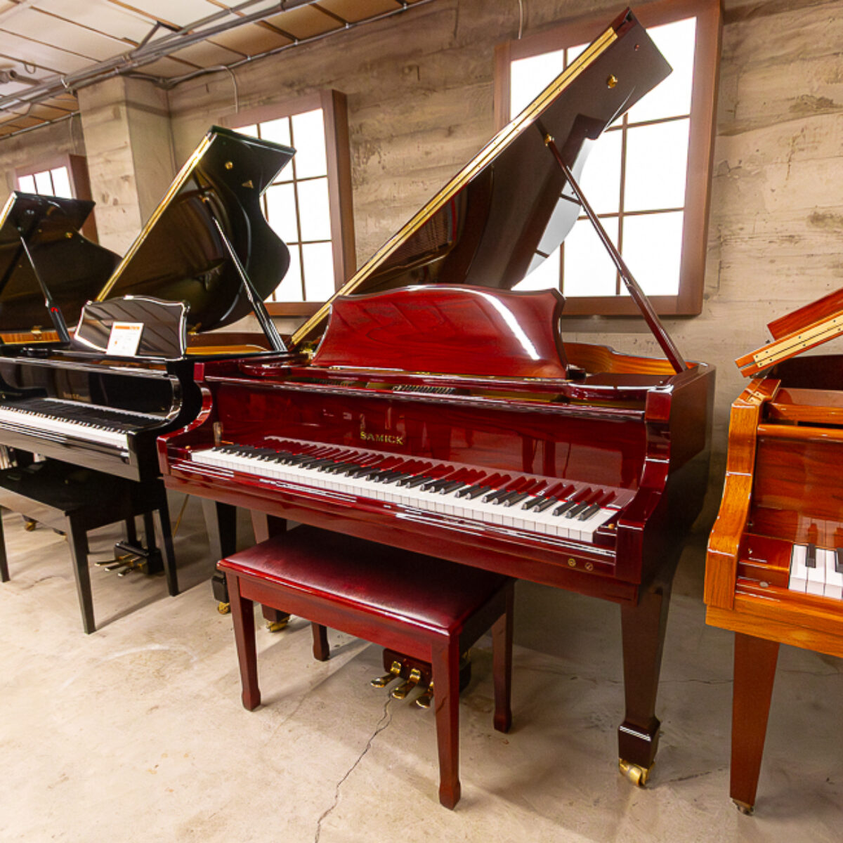 Samick mahogany baby grand piano with polished finish and matching bench showcased in showroom.