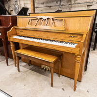Classic upright piano in natural oak finish, featuring a decorative lid and wooden piano bench, ideal for any music enthusiast.