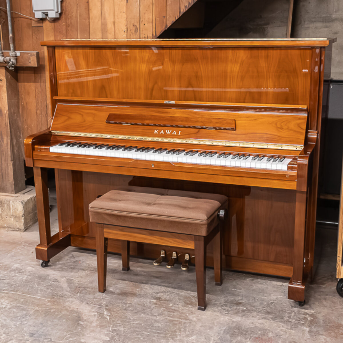 Alt text: Kawai upright piano featuring a polished mahogany finish and a matching bench, showcasing craftsmanship and elegance.