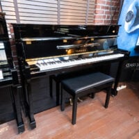 Yamaha upright piano in polished ebony finish, featuring premium keys and a matching bench, ideal for any music enthusiast.